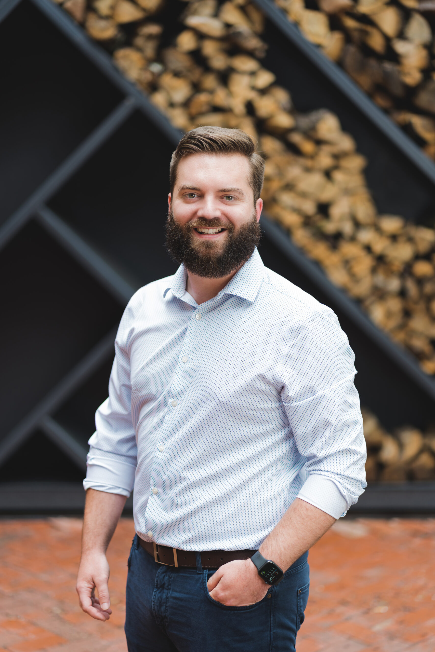 a man with a beard standing in front of a pile of wood